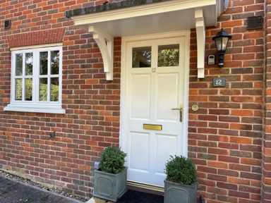 A white front door with two windows and a brass letterbox surrounded by red brick walls with two potted plants on either side