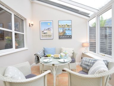 A small sunroom with wicker chairs and a table set with fruit and tea at Bluebelle Cottage Peasenhall