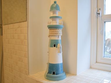 A decorative lighthouse on a tiled windowsill next to a window in a bathroom at Bluebelle Cottage Peasenhall