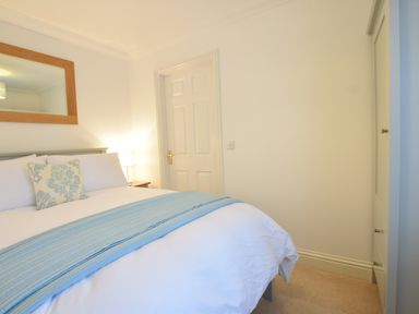 A bedroom with a bed featuring white bedding and a light blue throw and cushion a bedside table with a lamp a door and a wardrobe at Bluebelle Cottage Peasenhall