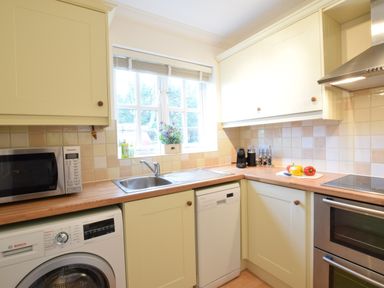 A kitchen with a washing machine microwave sink dishwasher oven stove and a window with flowers at Bluebelle Cottage Peasenhall