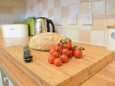 A kitchen countertop with a bread loaf cherry tomatoes and a knife at Bluebelle Cottage Peasenhall