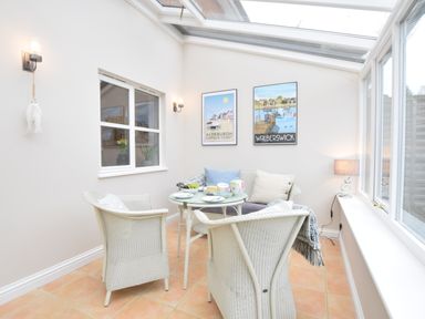 A conservatory with wicker chairs around a small round table and framed coastal posters on the wall at Bluebelle Cottage Peasenhall