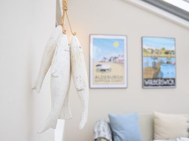 A room with hanging wooden fish decorations and framed coastal prints on a wall at Bluebelle Cottage Peasenhall