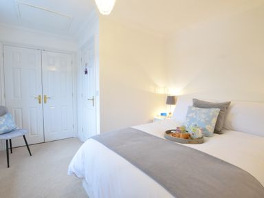 A bedroom with a bed with pillows and a tray with tea and croissants a chair and double doors at Bluebelle Cottage Peasenhall