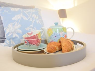 A tray with a teapot cups plates and croissants on a bed with cushions at Bluebelle Cottage in Peasenhall