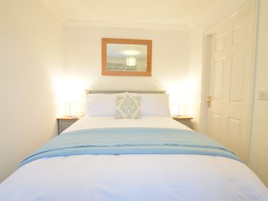 A bedroom with a bed with white sheets and a blue blanket and two bedside tables with lamps and a mirror on the wall at Bluebelle Cottage Peasenhall