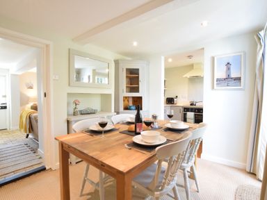 A dining area with a wooden table set for four with white chairs near a kitchen at Satis Cottage Westleton