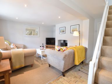 A sitting room with two sofas a white coffee table a television and stairs at Satis Cottage Westleton