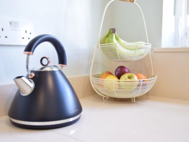 A black kettle next to a two-tier fruit basket with bananas and various fruits on a kitchen counter at Satis Cottage Westleton