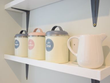 Metal containers labeled sugar coffee and tea with lids and a white ceramic pitcher on a white shelf at Satis Cottage Westleton