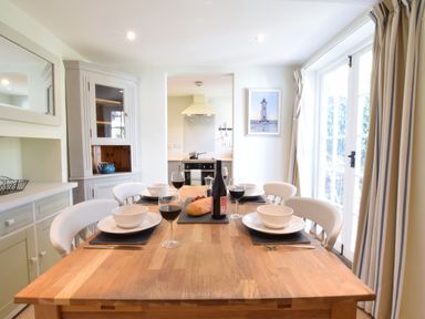A dining table set with bowls and wine glasses in a kitchen dining area with large windows and curtains at Satis Cottage Westleton