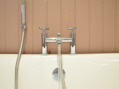 A bathtub with a silver faucet and a handheld showerhead against a paneled wall at Satis Cottage Westleton