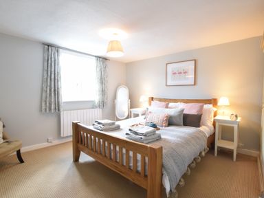 A bedroom with a wooden bed frame bedside tables and a standing mirror at Satis Cottage Westleton