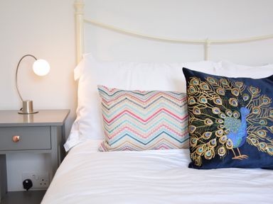 A bed with white sheets two decorative pillows and a bedside table with a lamp at Satis Cottage Westleton
