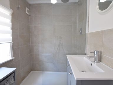 A bathroom with a shower area and a white sink with a faucet at Satis Cottage Westleton