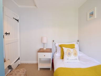 A small bedroom with a single bed yellow pillows and blanket a white nightstand with a lamp and a closed white door at Satis Cottage Westleton