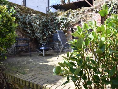 A small outdoor patio with chairs a fire pit and plants against a stone wall at Satis Cottage Westleton