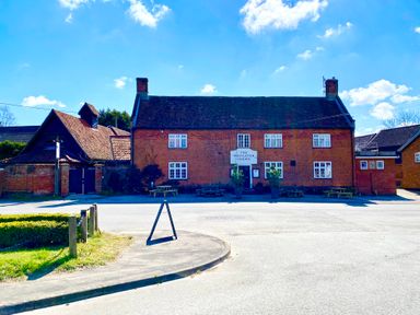 A brick building with a sign reading The Westleton Crown with picnic tables outside on a clear day at Satis Cottage Westleton