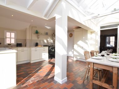 A kitchen and dining area with white cabinets wooden dining table and terracotta tile floor at Albion House Southwold