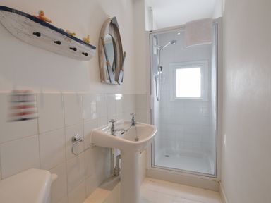 A bathroom with a pedestal sink a shower enclosure with a window and a small wooden boat shelf on the wall at Albion House Southwold