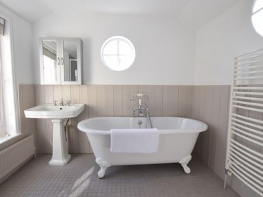 A bathroom with a freestanding bathtub with towel a pedestal sink a round window a mirrored cabinet and a towel radiator at Albion House Southwold