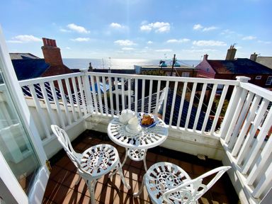 A small balcony with white metal table and chairs overlooking rooftops and the sea at Albion House Southwold