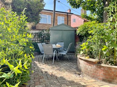 A garden patio with a table and six chairs in front of a green shed at Albion House Southwold