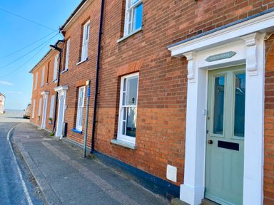 A row of brick houses with white window frames and green doors on a street at Albion House Southwold