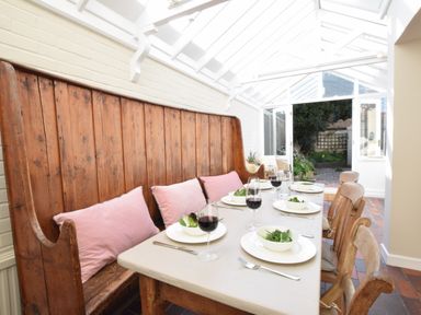 A dining area with wooden bench and chairs around a table set with bowls of salad and glasses of wine at Albion House Southwold