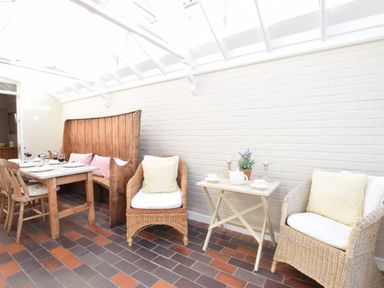 A bright conservatory with wooden dining table and chairs and wicker armchairs with cushions at Albion House Southwold