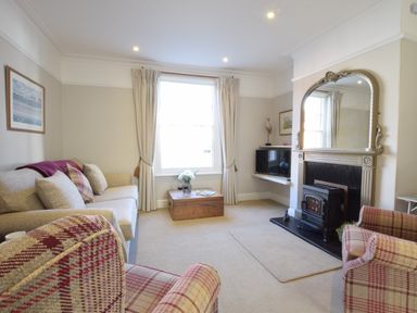 A living room with sofas chairs a wooden chest coffee table fireplace and television at Albion House Southwold