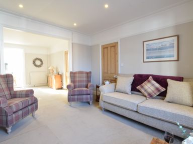 A living room with two plaid armchairs a beige sofa with cushions a wooden door and a cabinet with a lamp near the window at Albion House Southwold