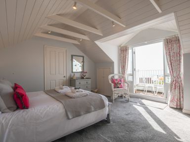 A bedroom with a bed, a dresser, a wicker chair, and an open door leading to a balcony at Albion House Southwold