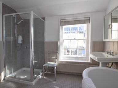 A bathroom with a glass shower enclosure a white chair a window a sink and a bathtub at Albion House Southwold