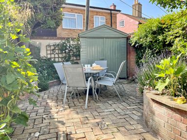 An outdoor patio with a table and chairs in front of a shed surrounded by plants and flowers at Albion House Southwold
