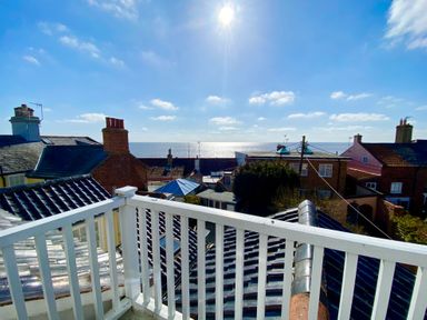 A balcony overlooking rooftops with chimneys and the sea in the background at Albion House Southwold