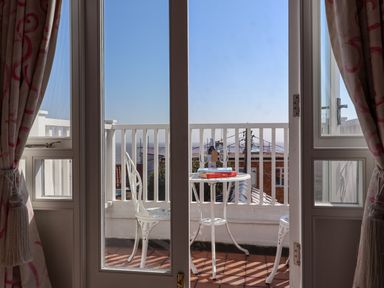 A balcony with a white table and two chairs with books, a bottle, and two glasses seen through glass doors at Albion House Southwold
