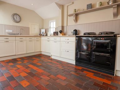 A kitchen with white cabinets a black stove and red and brown tile floor at Albion House Southwold