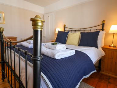A bedroom with a black metal bed frame navy bedding white towels and wooden bedside tables with lamps at Albion House Southwold