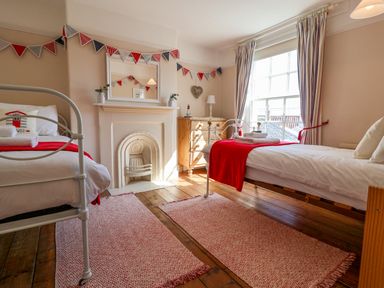 A bedroom with two single beds red blankets wooden chest of drawers and a window at Albion House Southwold