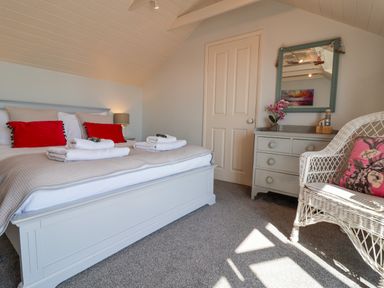 A bedroom with a double bed with red pillows white towels on it a wicker chair with a floral cushion a dresser with a mirror and flowers at Albion House Southwold