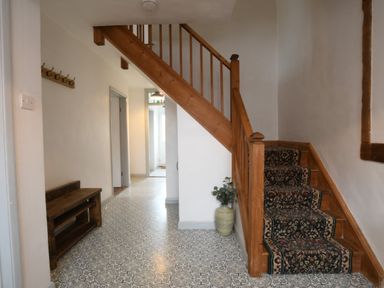 A hallway with a wooden staircase carpet runner a wooden bench hooks on the wall and a vase with a plant at Rosedene Rickinghall