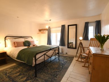 A bedroom with a bed a green blanket pillows a mirror a wooden chair a wooden dresser and blue curtains at Rosedene Rickinghall