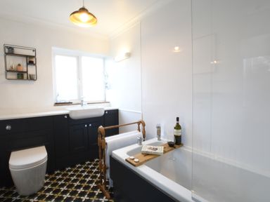 A bathroom with a bathtub holding a wine bottle glass and book at Rosedene Rickinghall