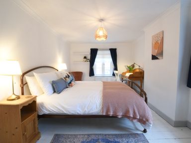 A bedroom with a metal bed frame a wooden nightstand lamps and a desk with a chair near a window with curtains at Rosedene Rickinghall