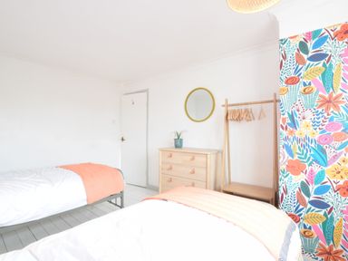 A bedroom with two single beds a wooden dresser a round mirror and a clothes rack with hangers at Rosedene Rickinghall