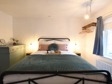 A bedroom with a bed with green blanket and pillows beside a dresser and a window with blue curtains at Rosedene Rickinghall