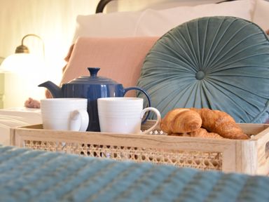 A tray with a blue teapot white cups and croissants on a bed with pillows at Rosedene Rickinghall