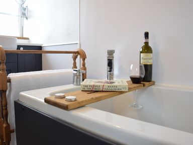 A bathtub with a wooden tray holding a book a bottle of wine and a glass of wine at Rosedene Rickinghall